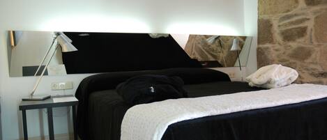 A bedroom with a bed, a nightstand, a lamp, and a stone wall.