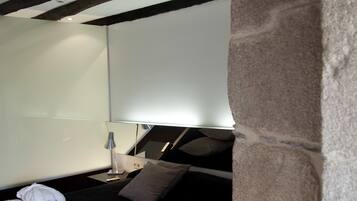 Ein modernes Schlafzimmer mit einem Steingewölbe, einem Bett mit weiß-schwarzem Überwurf, einem Nachttisch mit Lampe und einem großen Spiegel an der Wand.