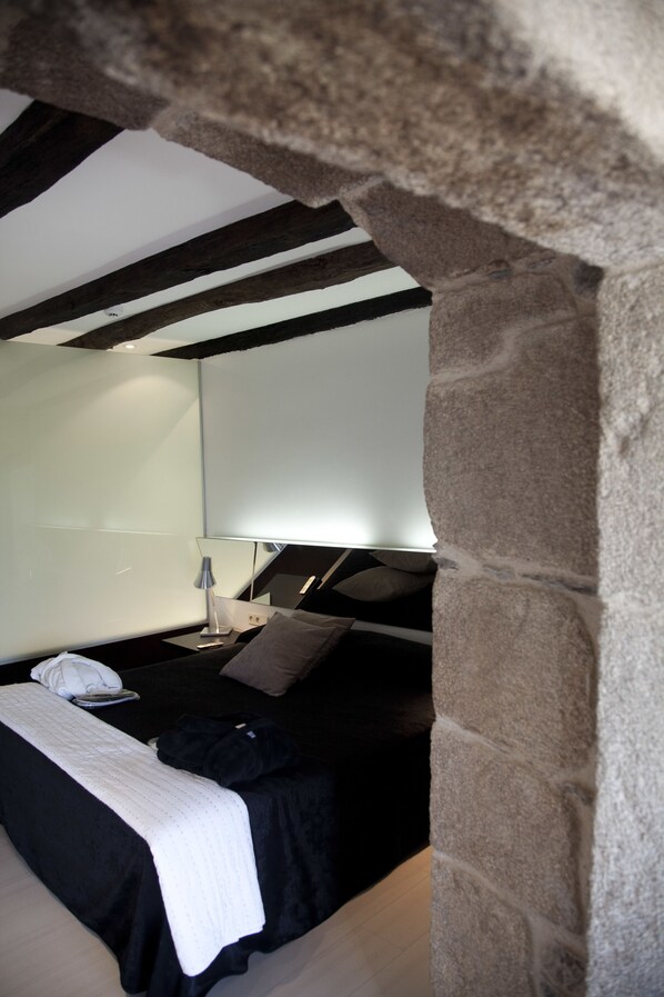 Een moderne slaapkamer met een stenen boog, een bed met een zwart-witte dekbedovertrek, een nachtkastje met een lamp en een grote spiegel aan de muur.