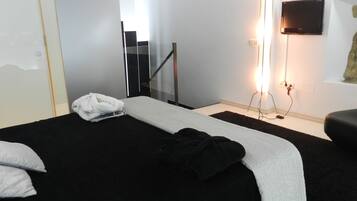 Habitación de hotel con cama, televisor de pantalla plana en la pared, escalera y ventana con vistas.