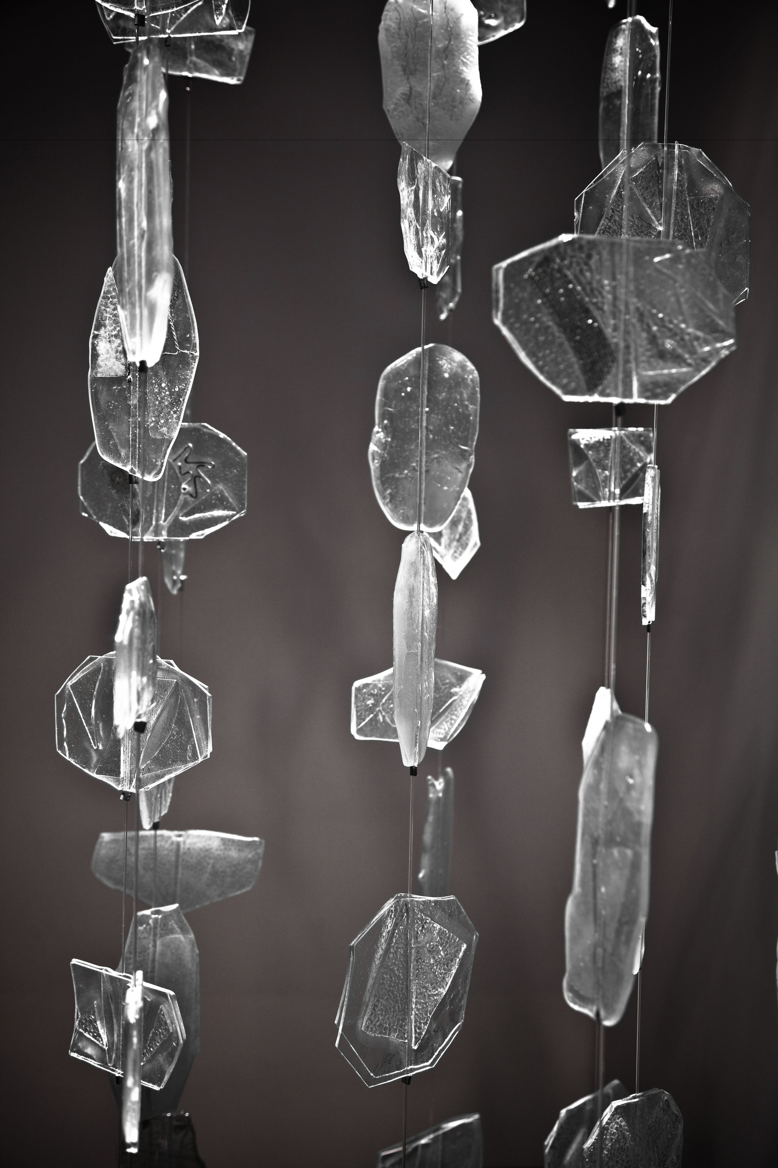 Una serie de adornos de cristal geométricos y transparentes, colgados de una barra central, reflejan la luz y crean un patrón de formas sobre un fondo oscuro.