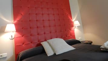 Una habitación de hotel con un cabecero rojo capitonado, dos lámparas de noche, una cama con ropa de cama oscura y una mesita de noche pequeña con un control remoto.