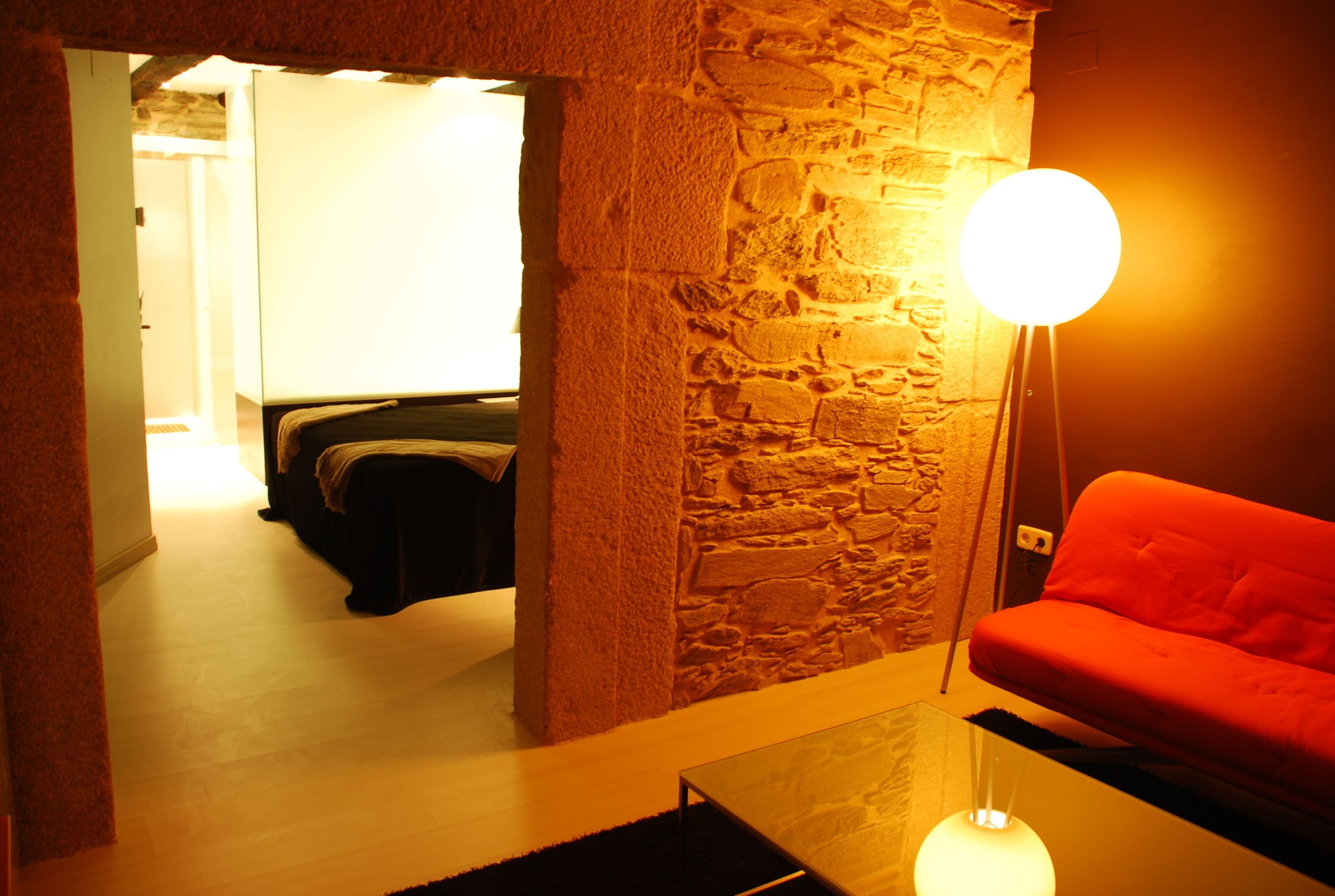Una habitación acogedora con pared de piedra, un sofá rojo y una mesa redonda con lámpara.