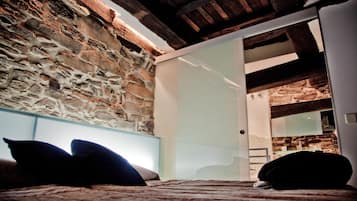 A bedroom with a stone wall, a bed with pillows, and a sliding door leading to another room.