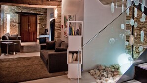 Un salon moderne avec un mur en pierre, une porte en bois, une bibliothèque blanche et un escalier agrémenté d’éléments en verre suspendus.