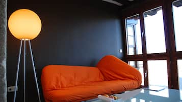 Una habitación moderna con una pared oscura, un sofá naranja brillante, una mesa de centro de cristal y una lámpara de pie.