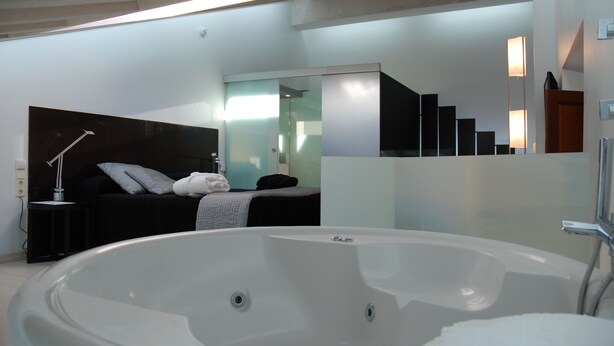 Une salle de bain moderne dotée d’une grande baignoire, d’une douche séparée et d’une chambre à coucher avec un lit et une table de chevet.