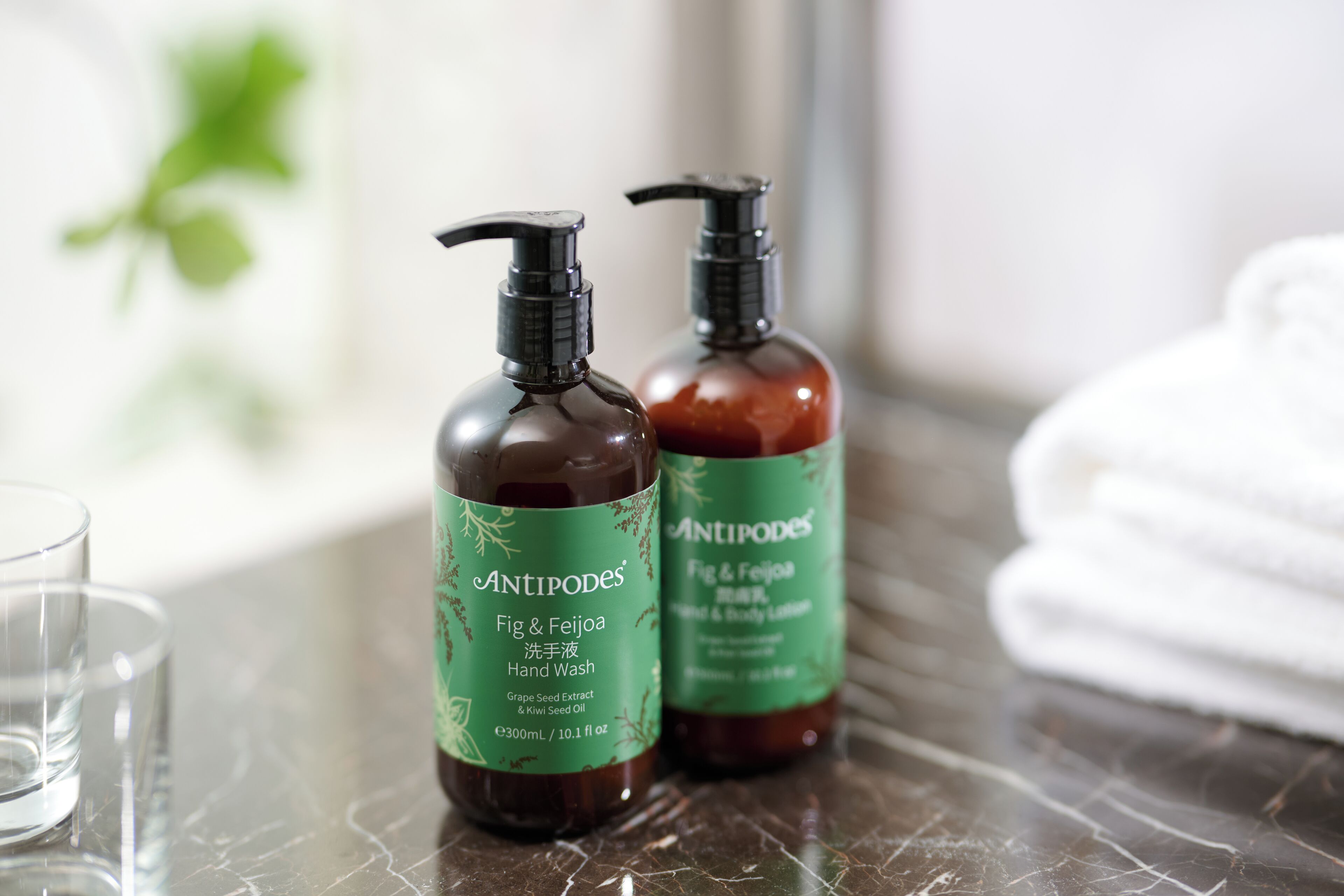 Two bottles of Antipodes Fig & Feijoa Hand Wash on a marble countertop.
