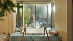 Ein Badezimmer mit Badewanne, einem Fenster mit Blick auf Grünflächen und einem Korbwäscher mit Handtüchern.