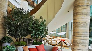 A spacious lobby with a modern design, featuring a large seating area with a sofa and ottoman, a coffee table, and a large tree. - The Royal Garden Kowloon East (Sai Kung)