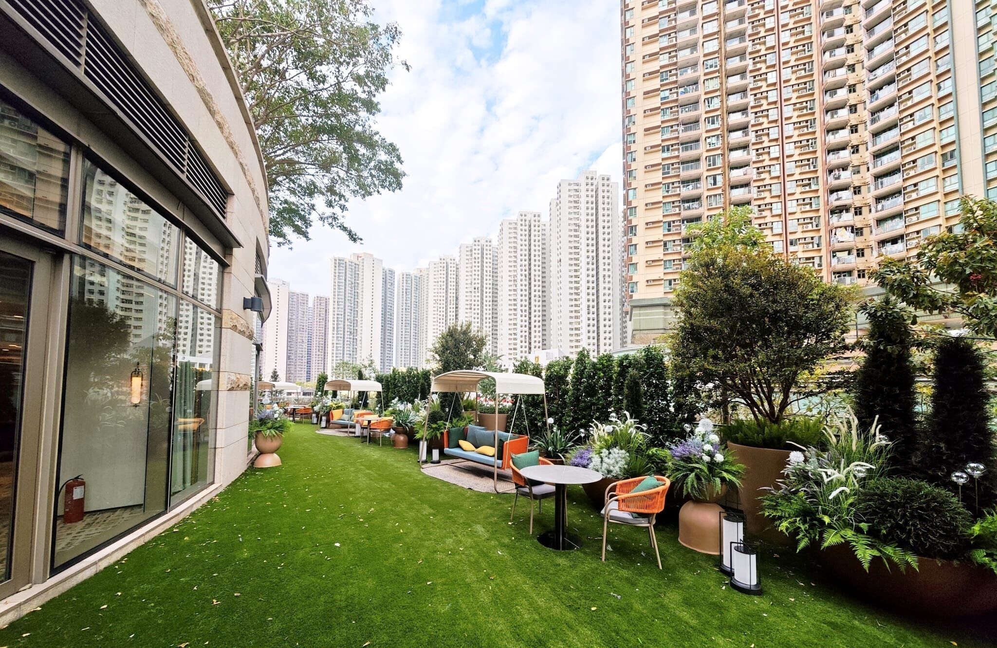 A courtyard with a lawn, outdoor seating, and tall residential buildings in the background.