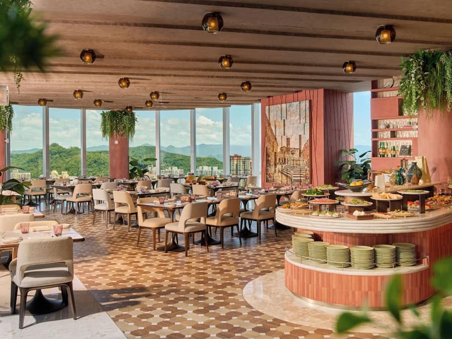 A restaurant with a view of mountains, multiple dining tables, and a buffet area.