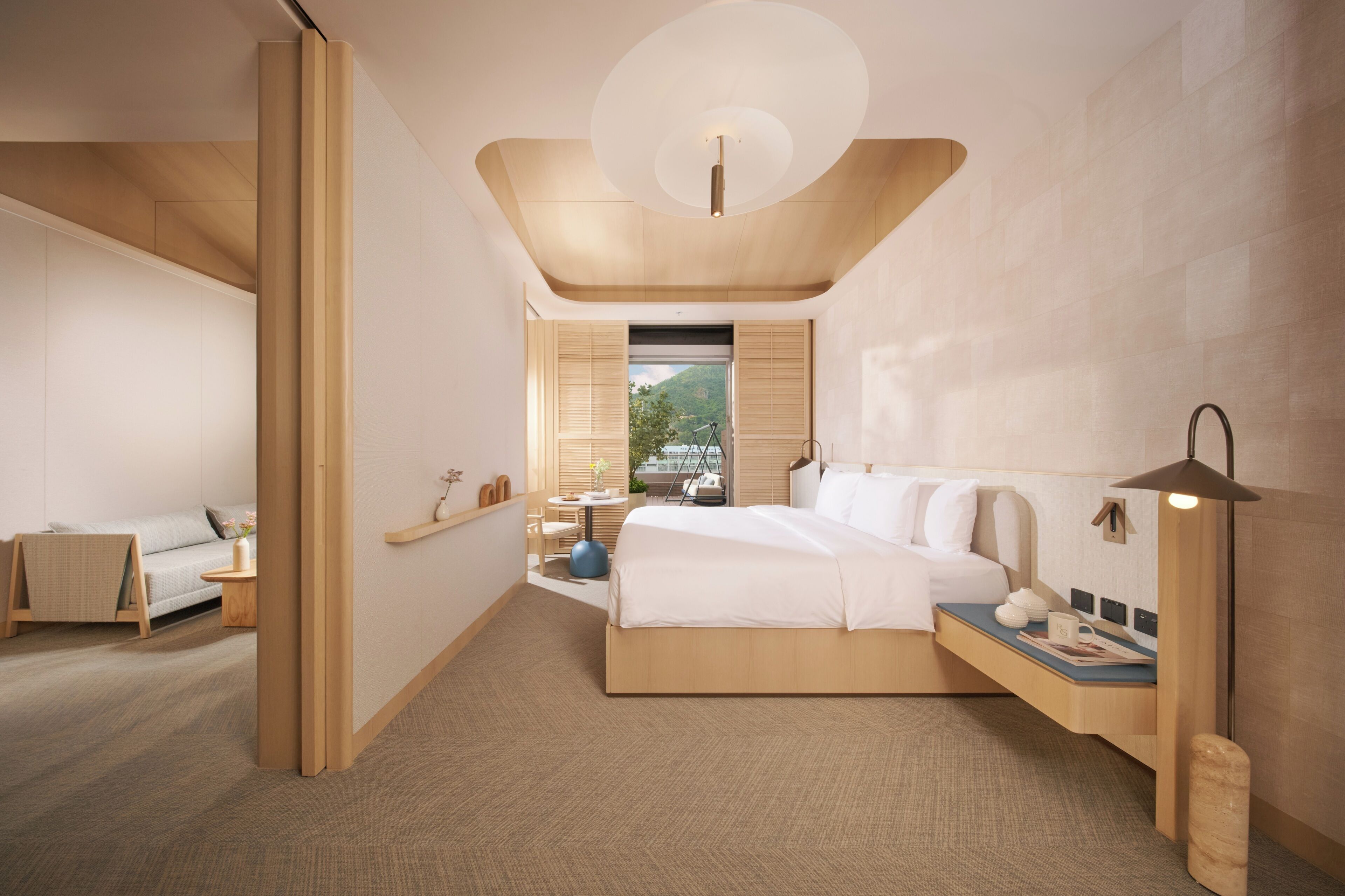 A modern bedroom with a large bed, bedside table, lamp, and a view of the outdoors.