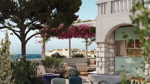 A rooftop terrace with outdoor seating, a stone wall, and a view of the sea. - Villa Orsula (Dubrovnik)