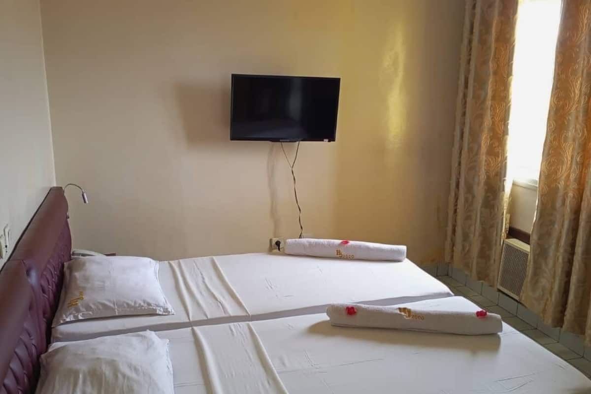A hotel room with a bed, a television mounted on the wall, and a window with curtains.