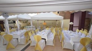 A banquet hall with tables set for a formal event, covered by white canopies, and chairs with yellow sashes. - Hotel Jouvence 2000 (Yaoundé)