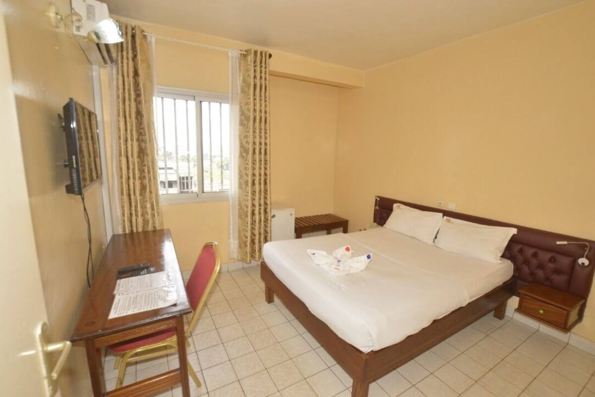 A hotel room with a bed, a desk, a chair, a TV, and a window with curtains.