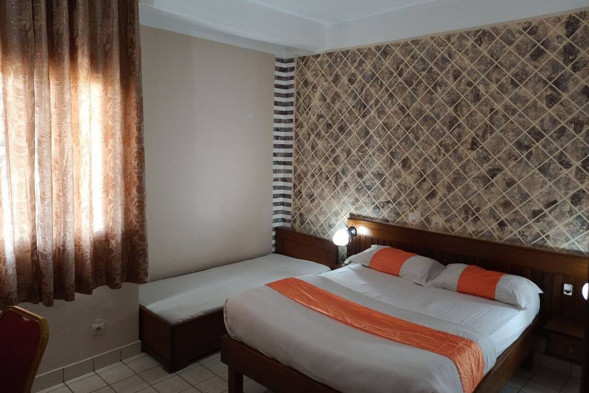A hotel room with a bed, a bedside table, a chair, and a patterned wall.