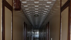A long, narrow hallway with doors on both sides, a tiled floor, and a patterned ceiling. - Hotel Jouvence 2000 (Yaoundé)