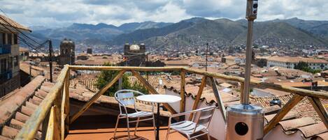 A terrace with a table and chairs, a heater, and a view of a cityscape with mountains in the background.