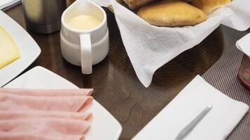 Een ontbijttafel met pannenkoeken, ham, een thermoskan en een fruitschaal.