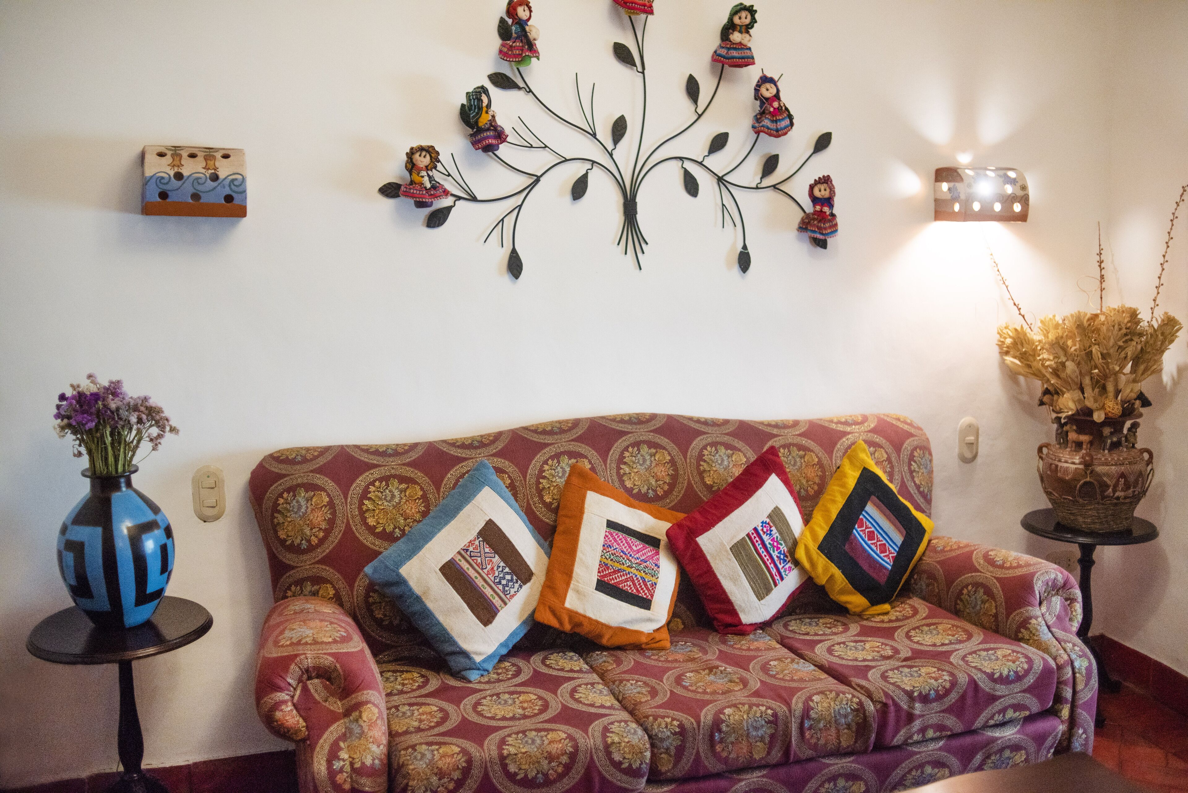 A living room with a patterned sofa, decorative pillows, a wall art piece, and a vase with flowers.