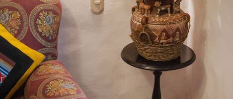 Un rincón con un sofá estampado, un jarrón decorativo con flores secas y una lámpara de pared.