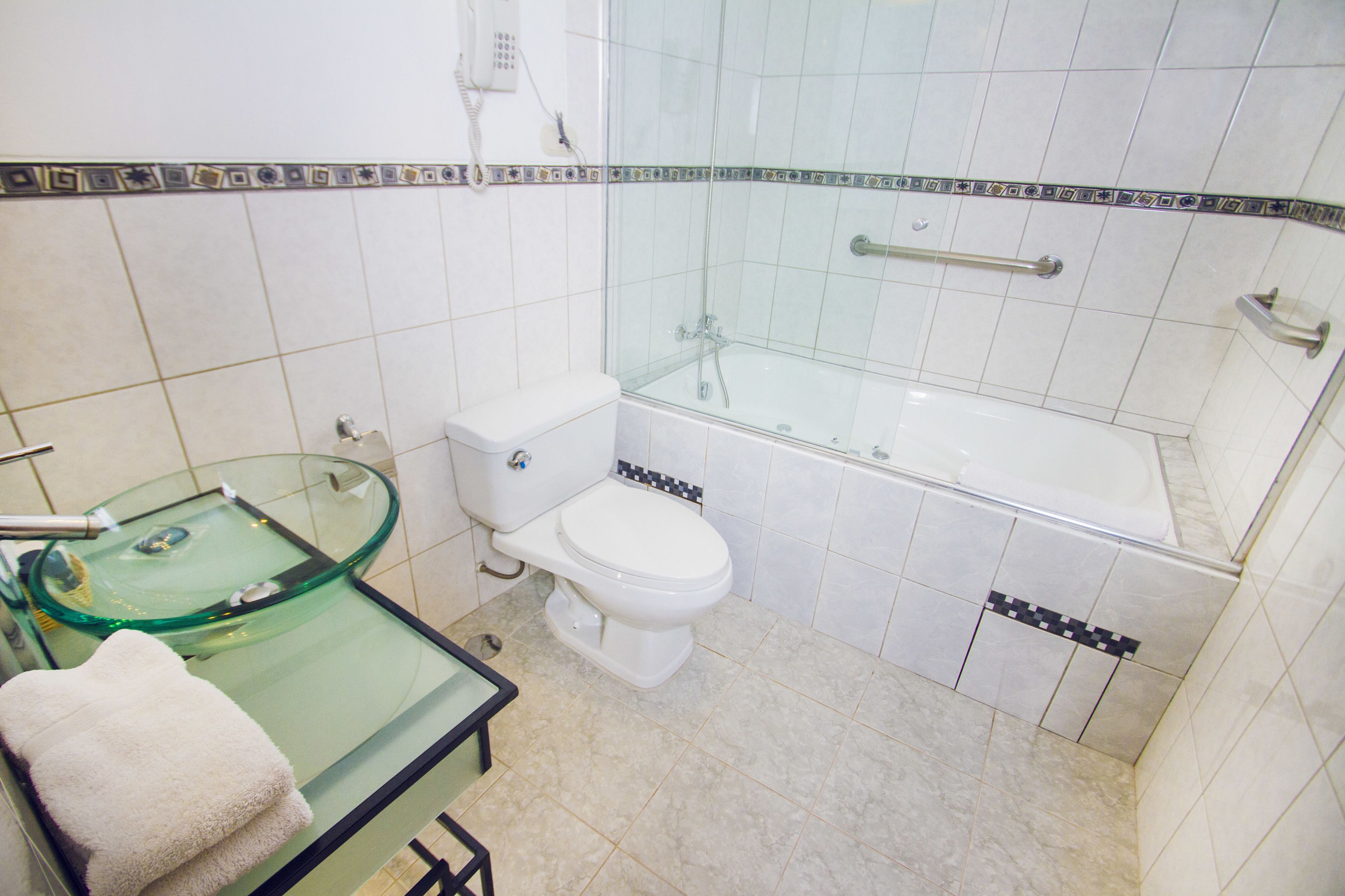 Un baño con cabina de ducha de vidrio, inodoro y lavamanos de vidrio.