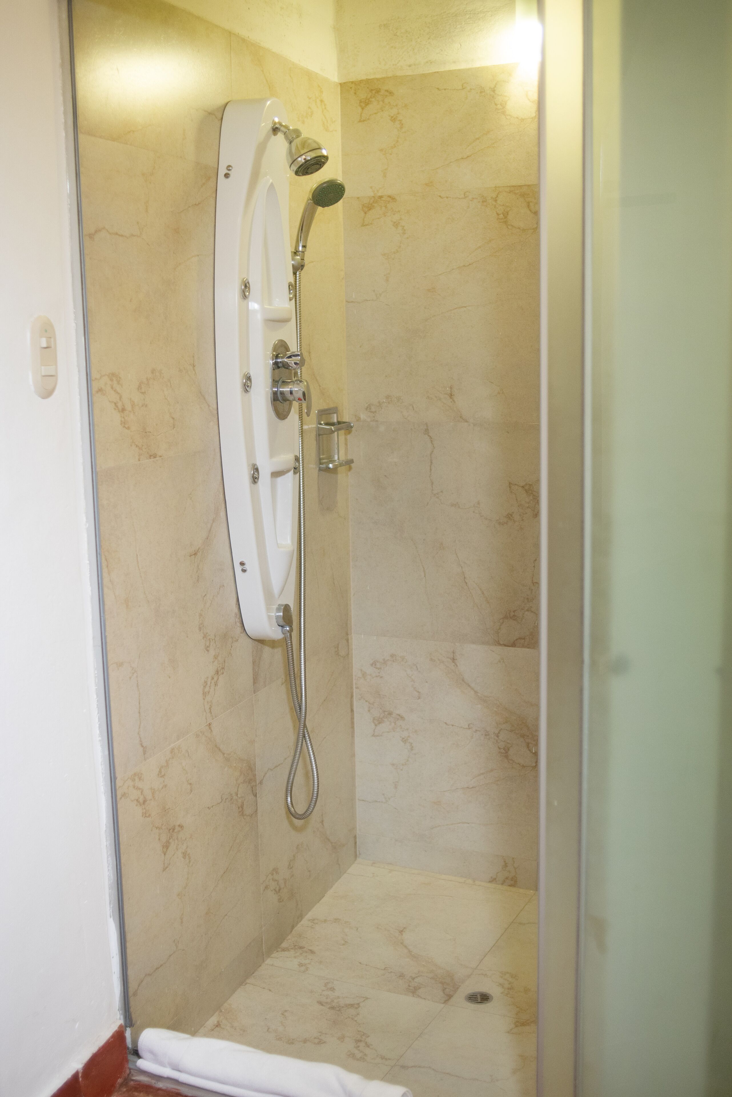 Une douche équipée d’un pommeau de douche à main et d’un robinet mural, avec des murs en marbre et un sol carrelé.