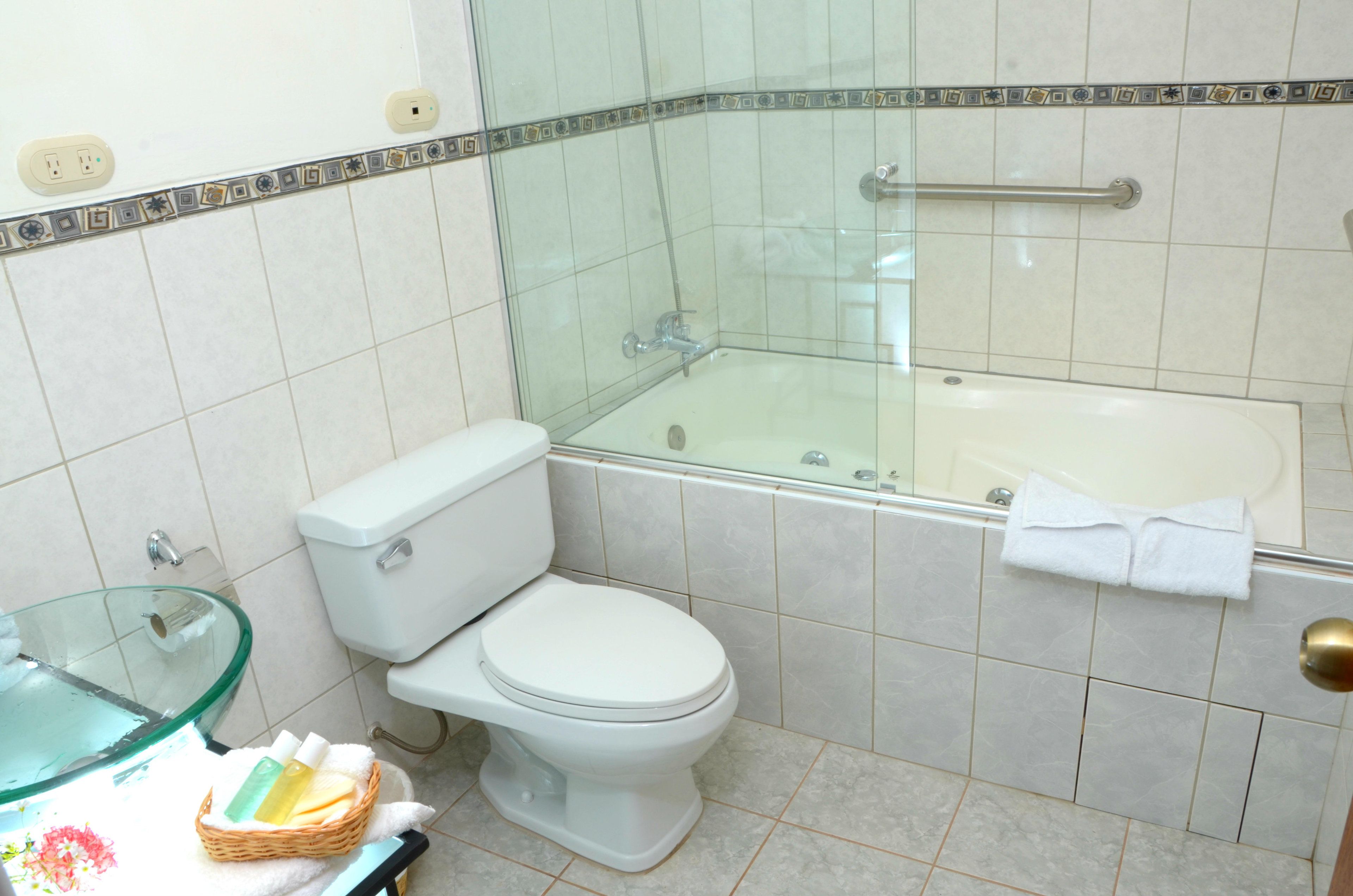 Un baño con ducha de vidrio, inodoro blanco y lavamanos de vidrio.