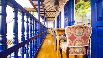 A corridor with blue railings, wooden flooring, and a patterned chair.