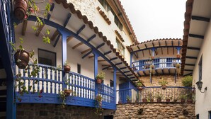 A traditional courtyard with stone walls, blue balconies, and hanging plants. - Rumi Wasi (Cusco)