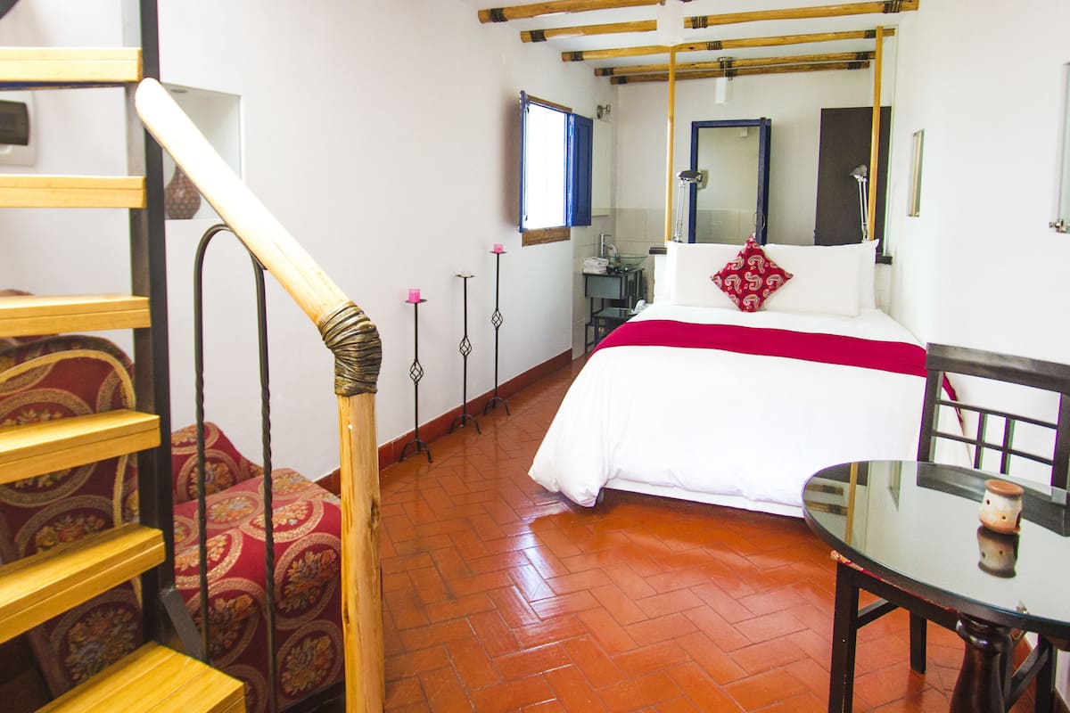 A bedroom with a bed, a chair, a table, and a mirror.