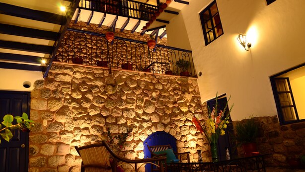 A stone wall with a blue door, a staircase with a railing, and potted plants. - Rumi Wasi (Cusco)