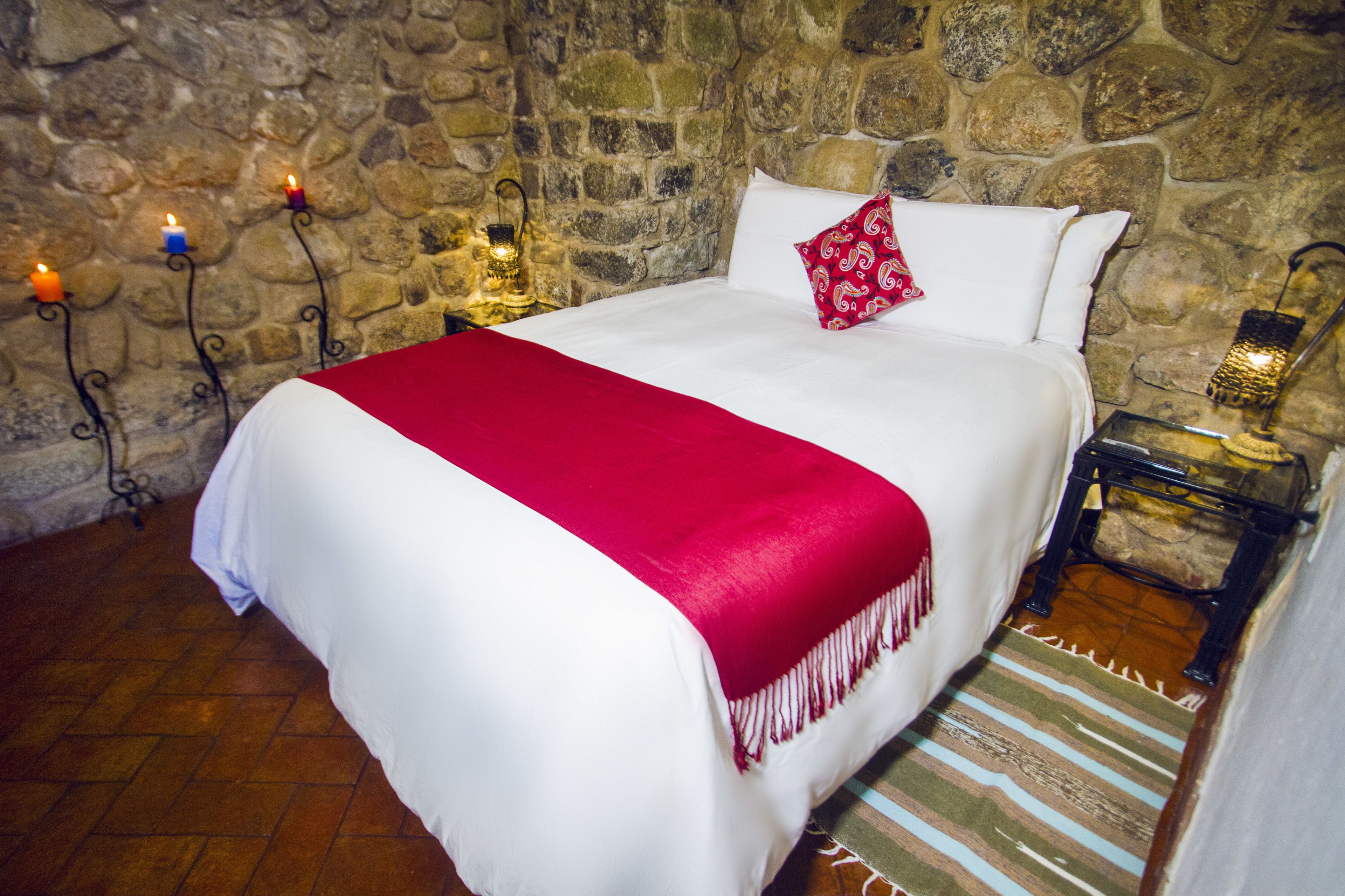 Un lit avec une couvre-lit blanche et rouge, un oreiller rouge et un tapis à rayures.