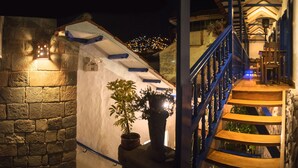 A stone wall with a small, illuminated structure and a staircase with blue railings. - Rumi Wasi (Cusco)