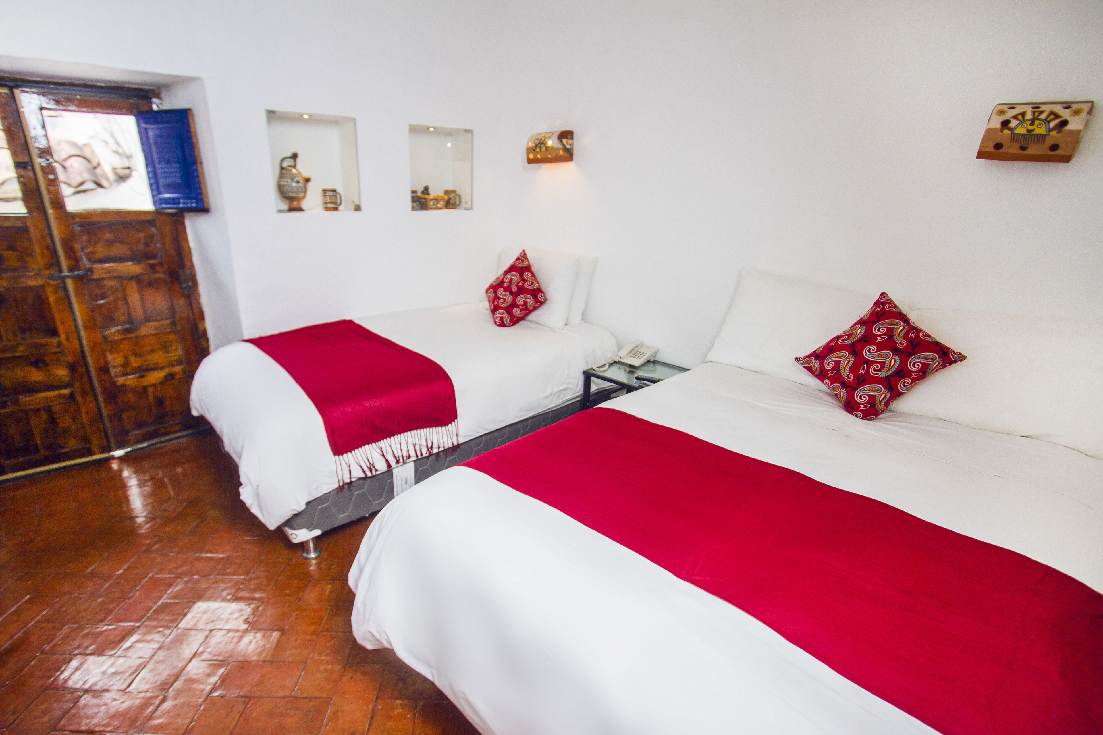 A hotel room with two beds, each with a white and red bedspread, and a wooden floor.