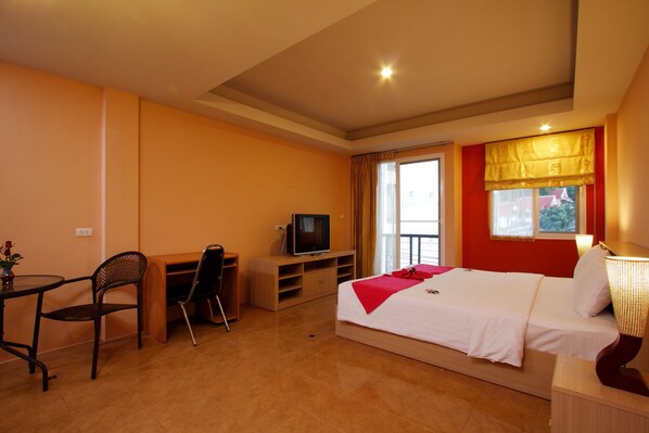 A hotel room with a bed, a desk with a television, a chair, and a window with curtains. - Blue Ocean Studio (Patong)