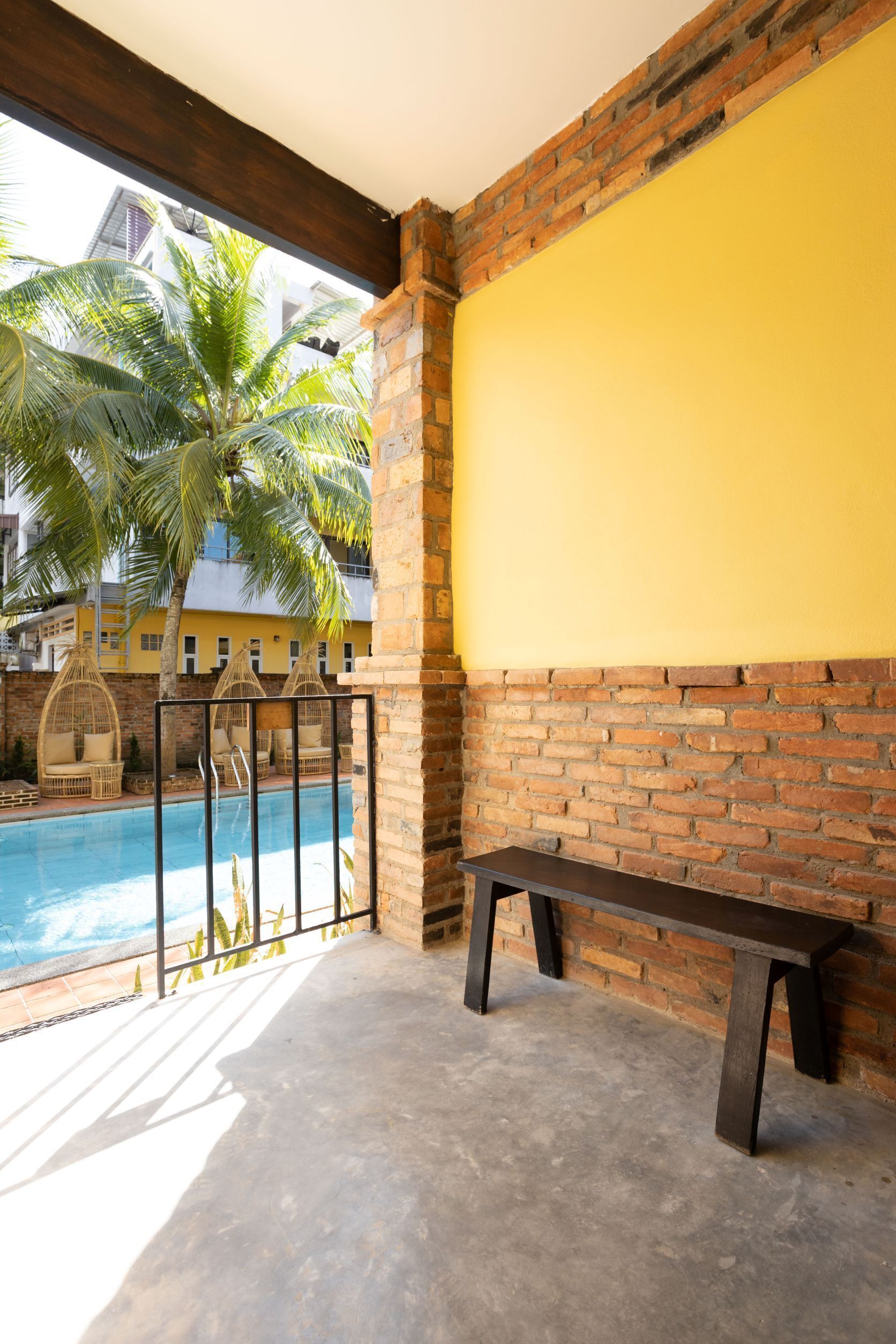 A balcony with a pool, a bench, and a view of palm trees and buildings.