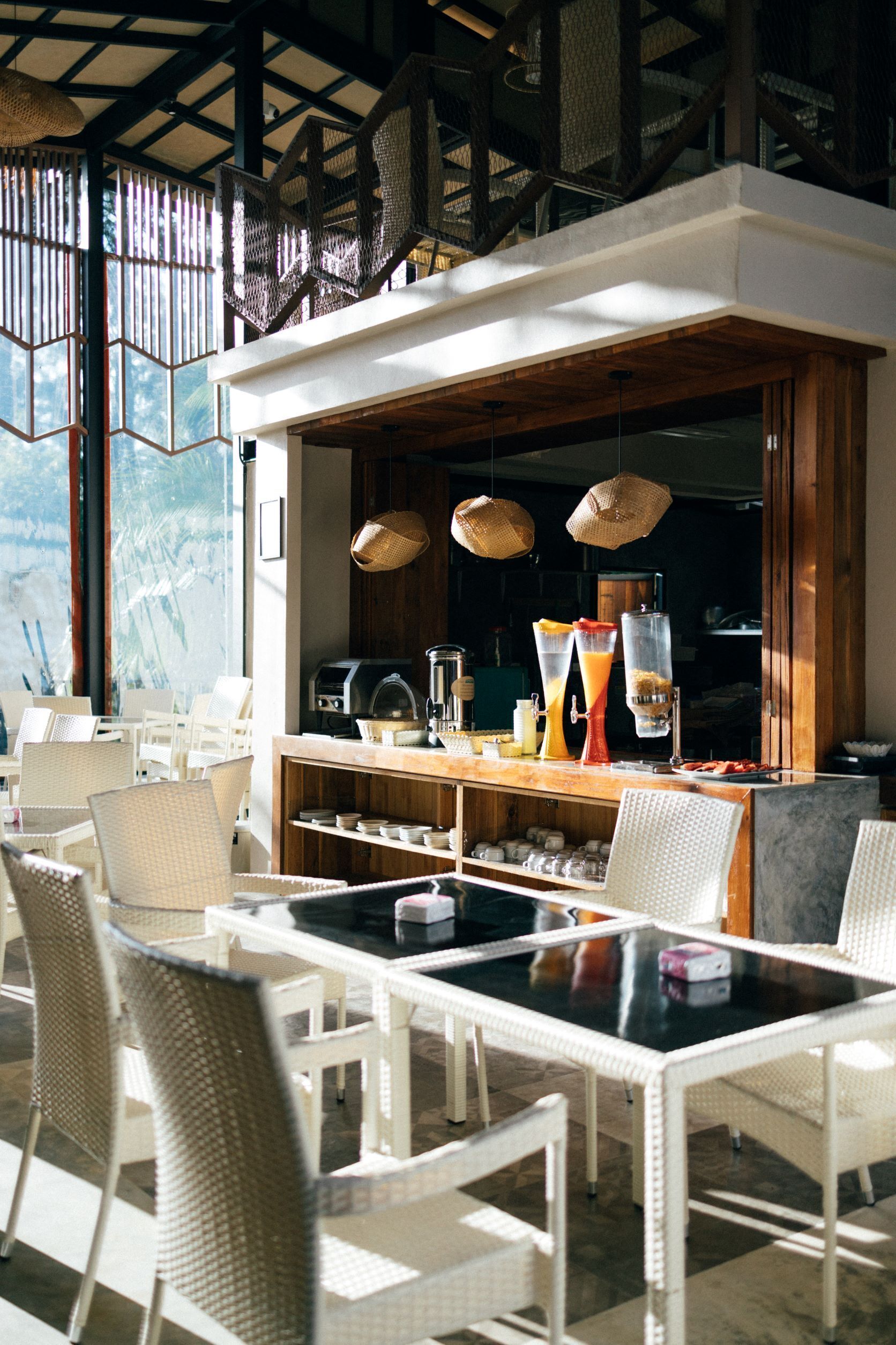 Un restaurante con mobiliario de mimbre blanco, una zona de bar con bebidas y vistas al exterior.