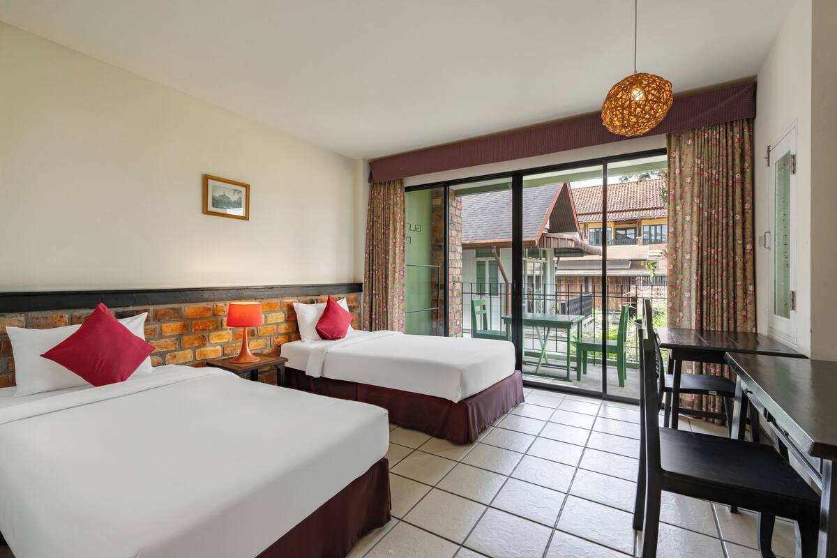 A hotel room with two beds, a desk, and a view of the outside.