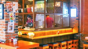 A restaurant with a brick wall, wooden counter, and stools. - Motive Cottage Resort (Takua Pa)