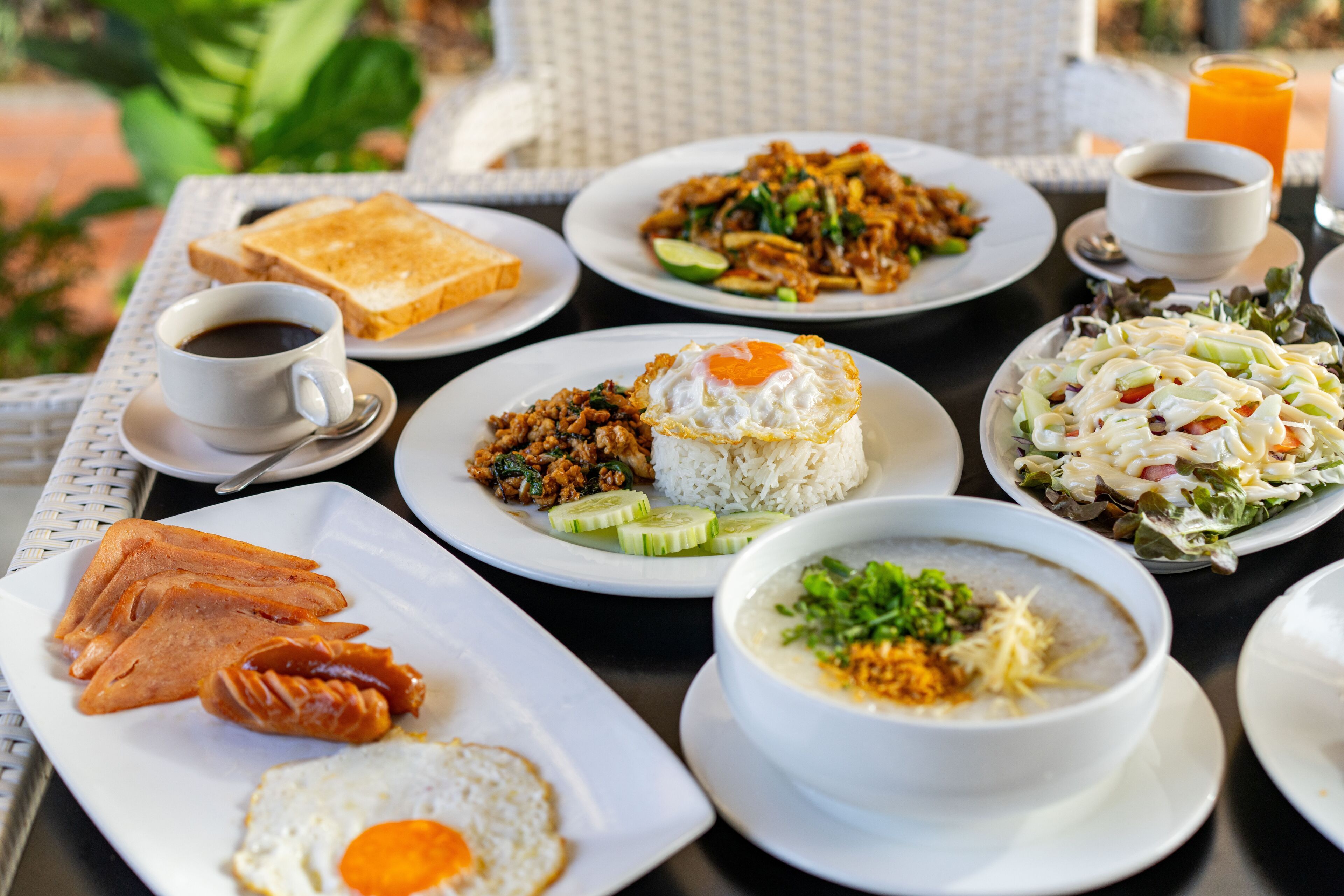 Una mesa servida con diversos platos, incluyendo arroz, huevos y una ensalada, junto con una taza de café y un vaso de jugo de naranja.