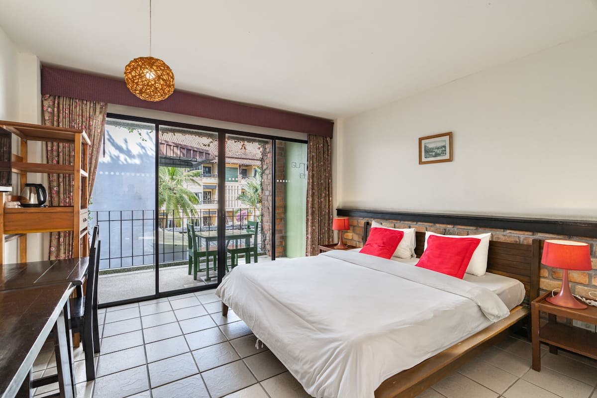 A hotel room with a bed, a desk, a chair, a table, a lamp, and a view of the outside.