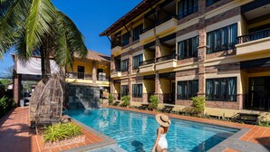 A swimming pool with a person standing at the edge, surrounded by a building with multiple balconies and a palm tree. - Motive Cottage Resort (Takua Pa)