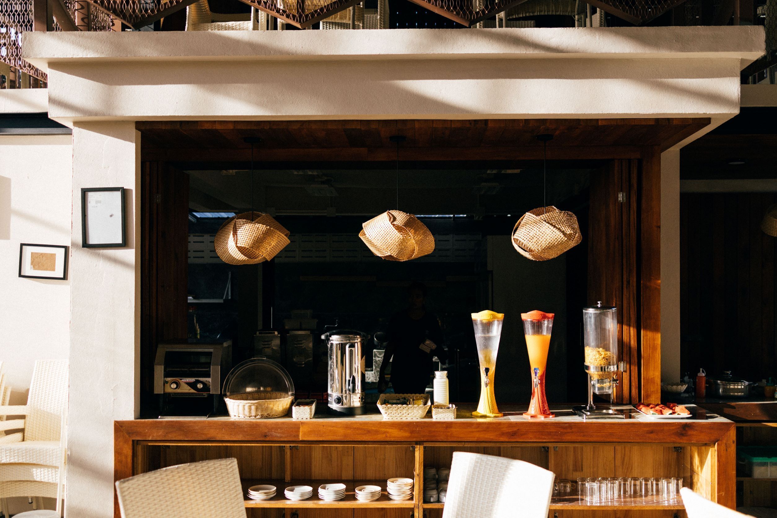Una zona de bar con cestas de mimbre colgando, una máquina de café y una mesa con desayuno que incluye un batido y un bol de fruta.