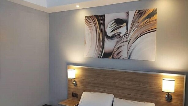 A modern hotel room with a large bed, two bedside tables with lamps, and a large abstract painting on the wall. - Hotel Meumi Palace (Yaoundé)