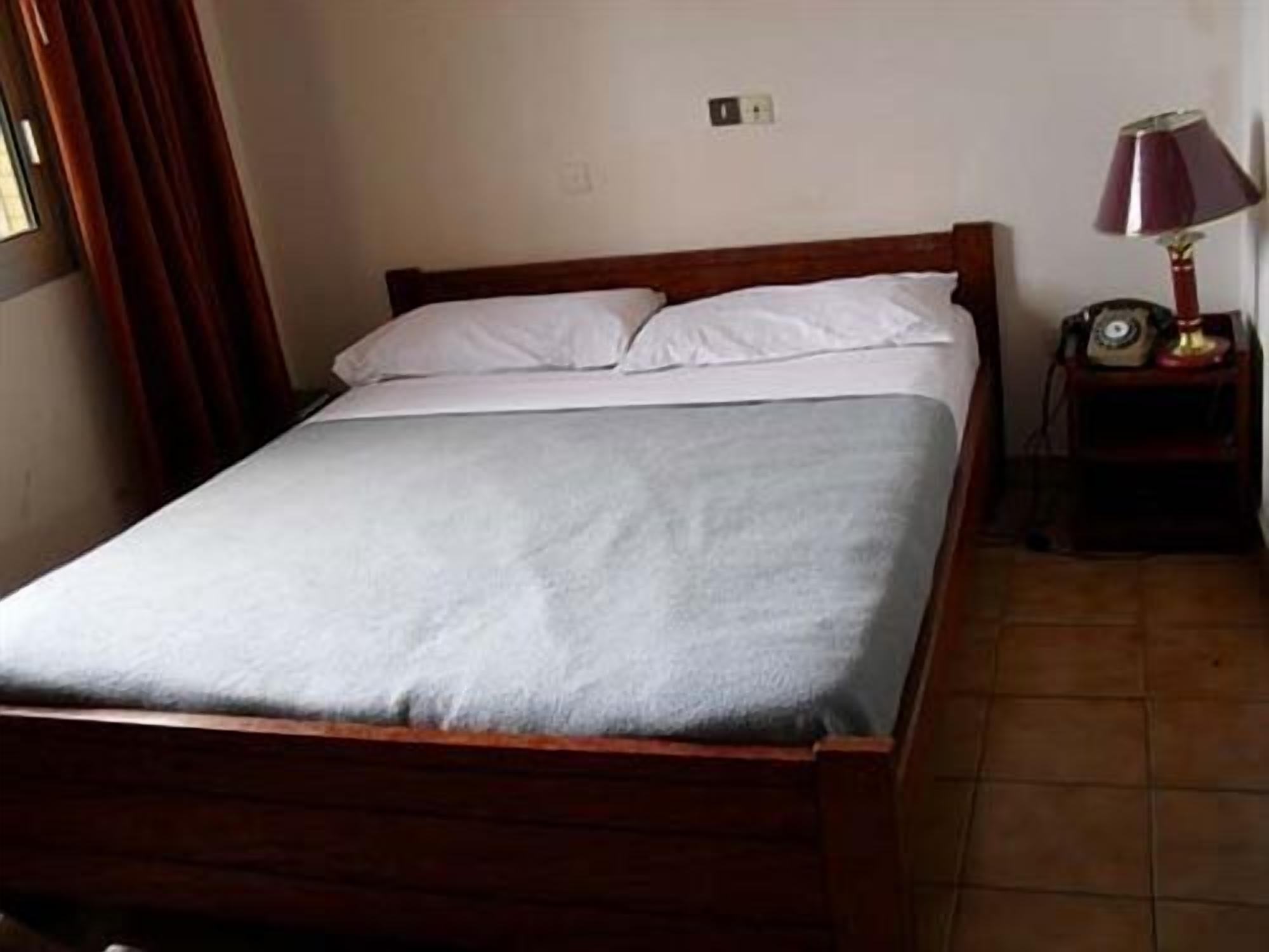 A single bed with a wooden frame and white bedding in a room with a tiled floor.