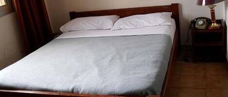 A single bed with a wooden frame and white bedding in a room with a tiled floor.