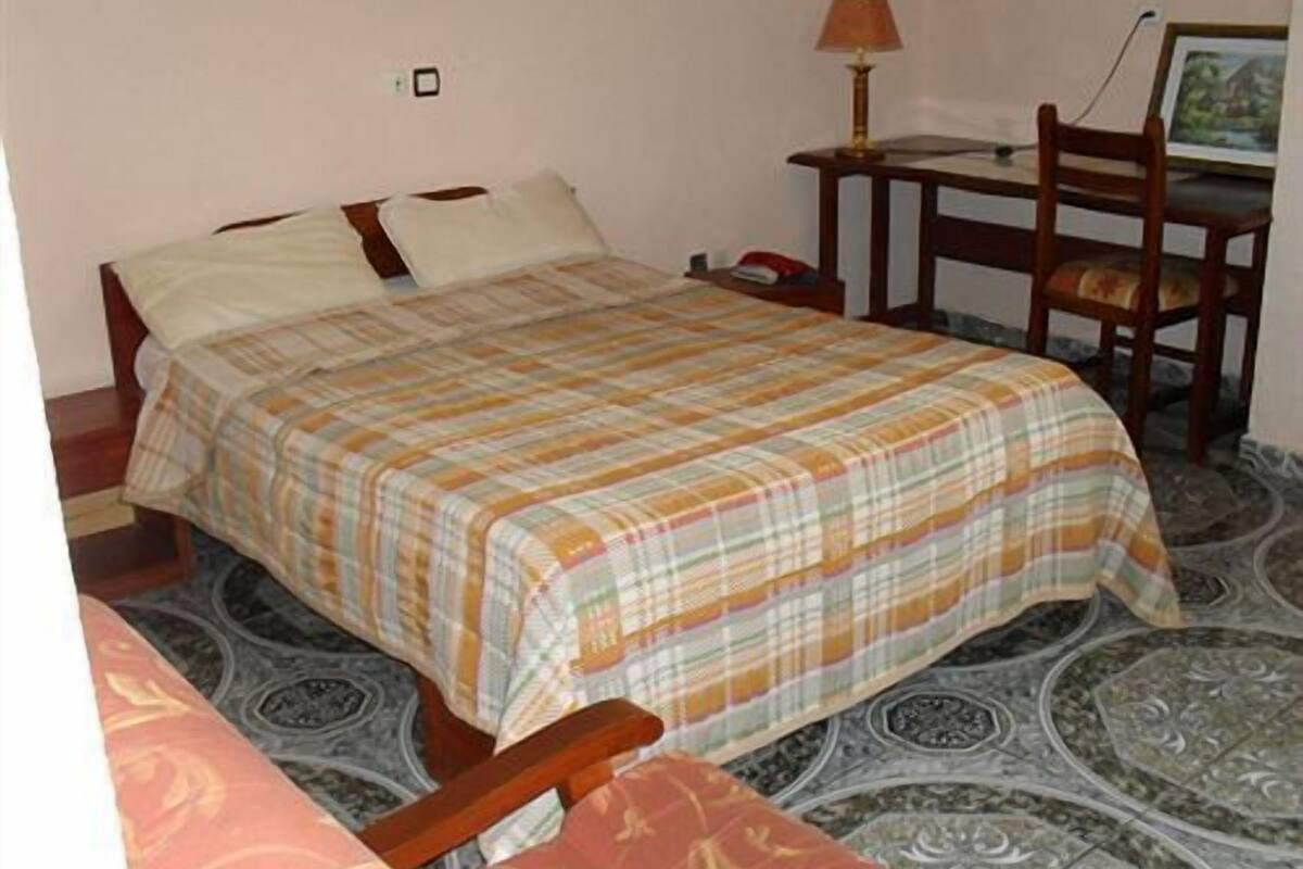 A bedroom with a bed, a chair, a desk, and a lamp.
